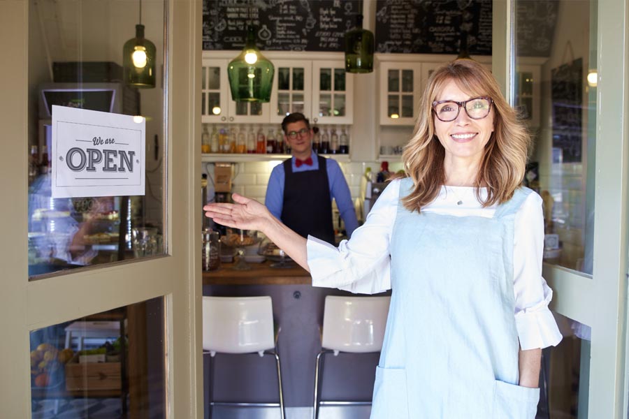 Business Insurance - Woman Business Owner Standing in Front of Her Shop Welcoming Customers In